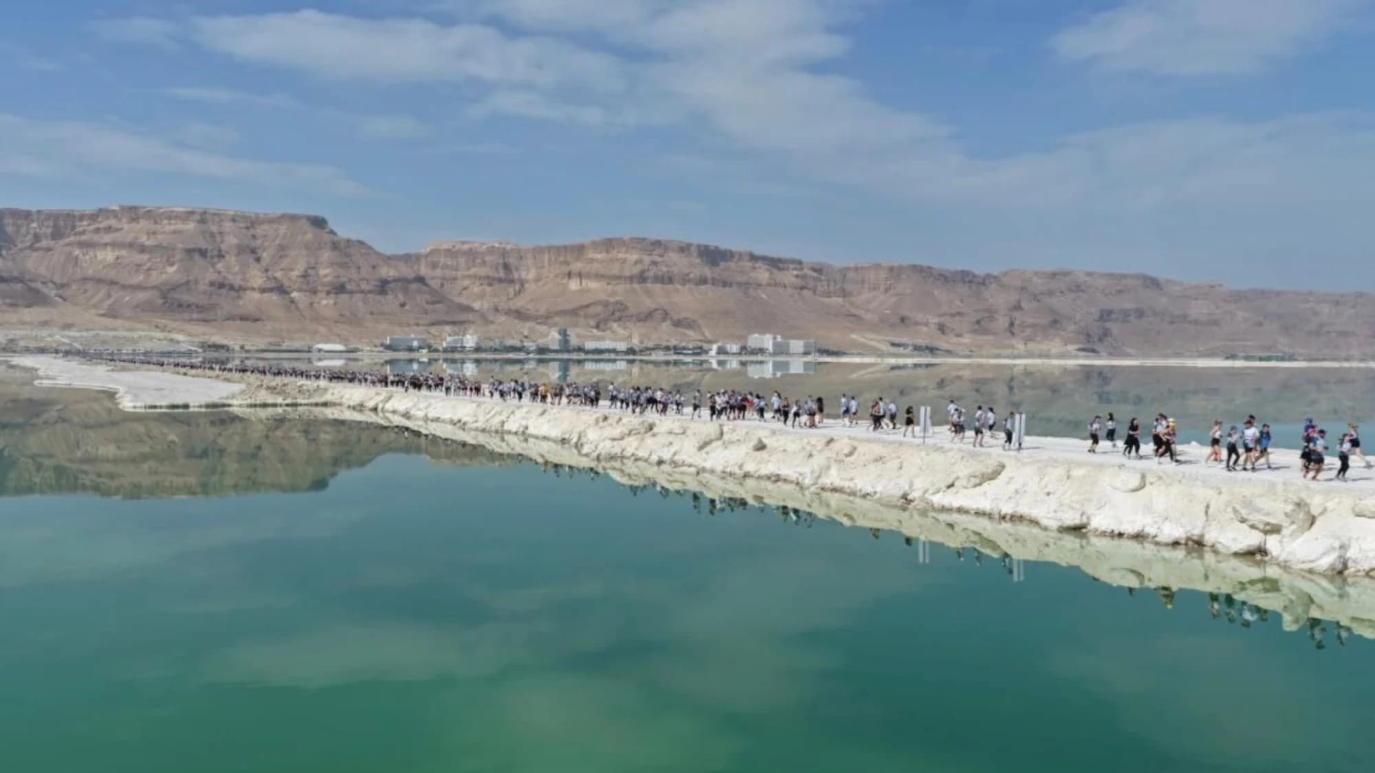 Hundreds of runners crossing the Dead Sea causeway between the water and the desert mountains