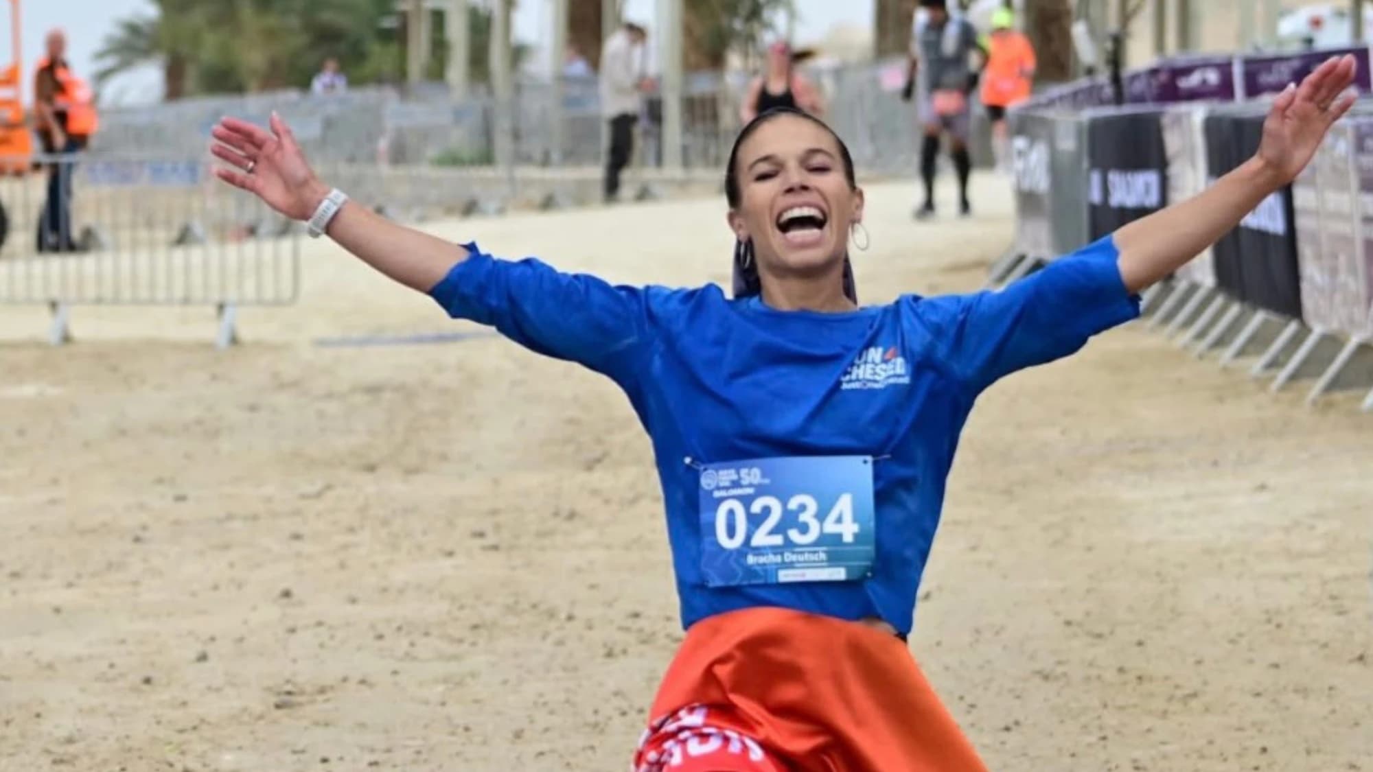 A Run 4 Chesed runner crossing the finish line with arms spread wide