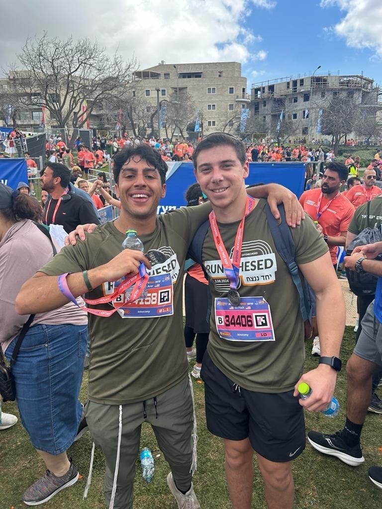 Two runners in Run Chesed shirts with their finisher medals after the race