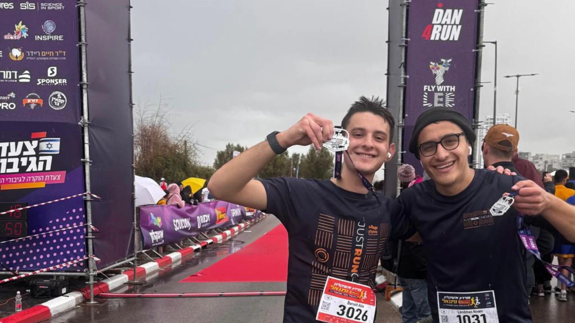 Two runners holding up their finisher medals in the rain at the Ashkelon race